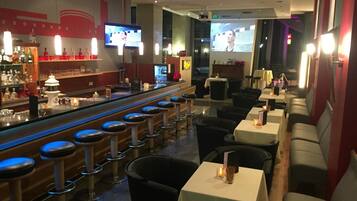 A bar area with stools, tables, and a TV screen displaying a program.