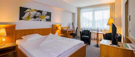 A hotel room with a large bed, a desk, a chair, a computer, and a painting on the wall.