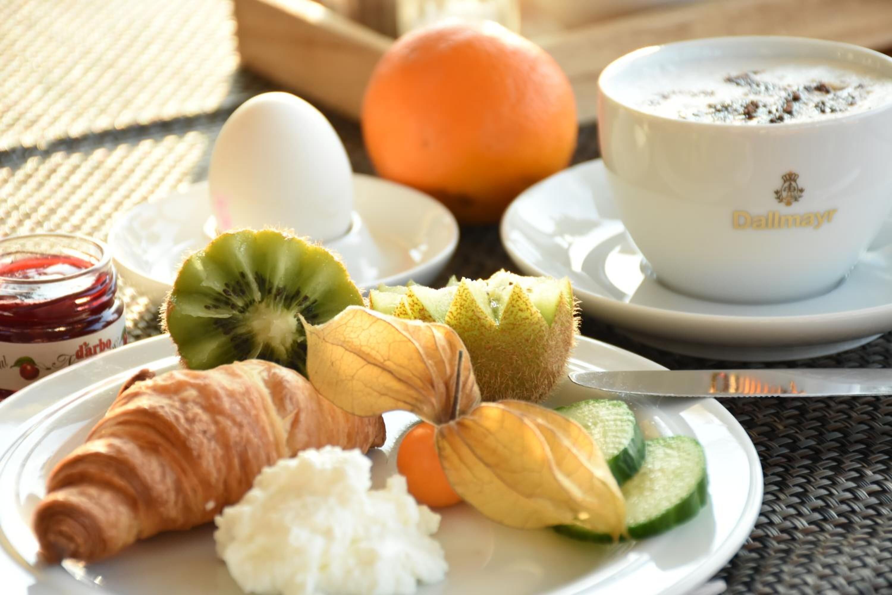 A breakfast plate with croissant, yogurt, kiwi, orange, and a cup of coffee.