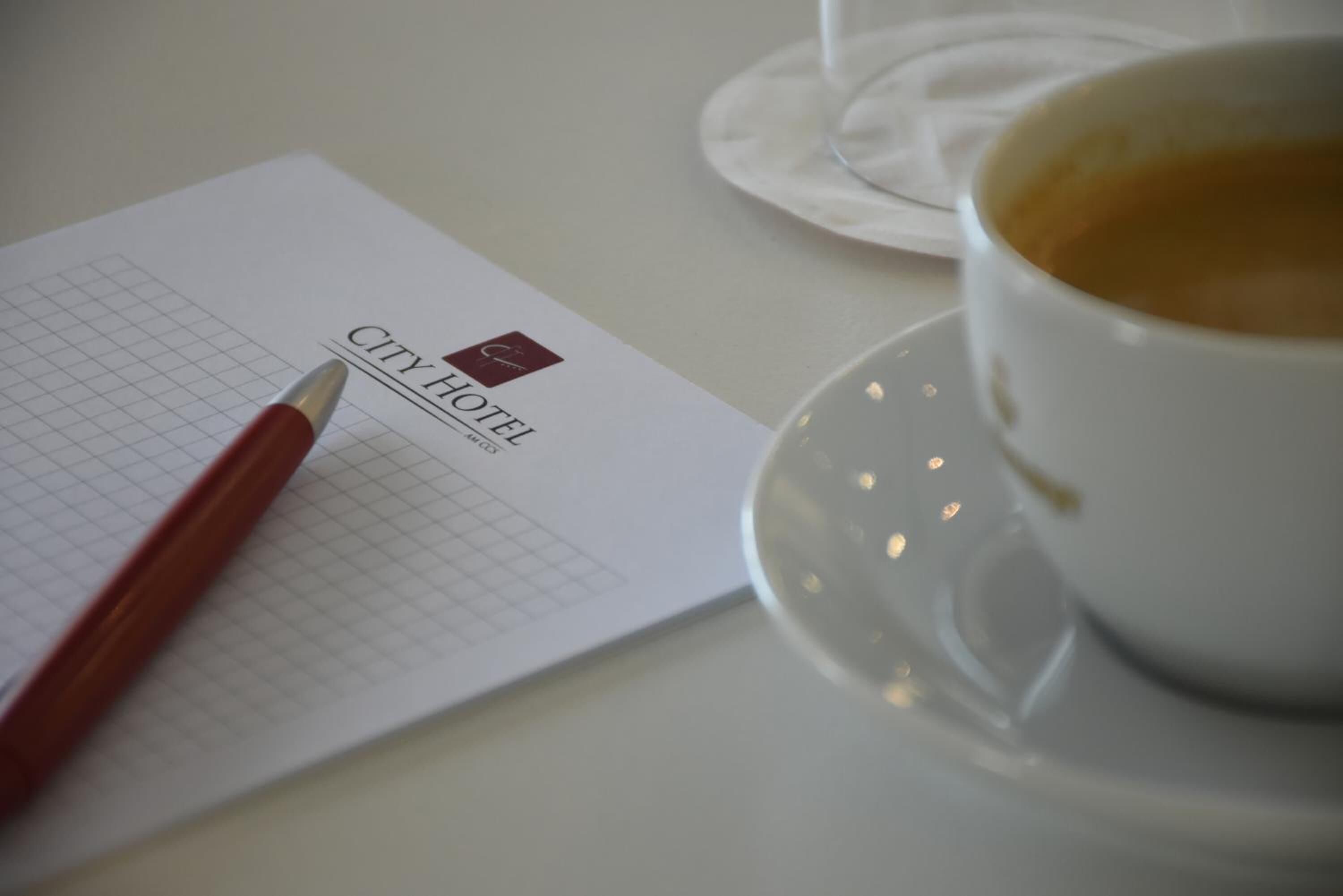 Um formulário de check-in de hotel com uma caneta, uma chávena de café e um guardanapo sobre uma mesa.