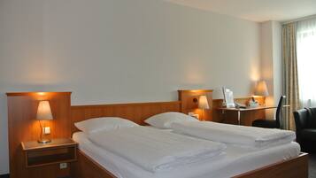 A hotel room with two beds, bedside lamps, a desk with a phone, and a chair.