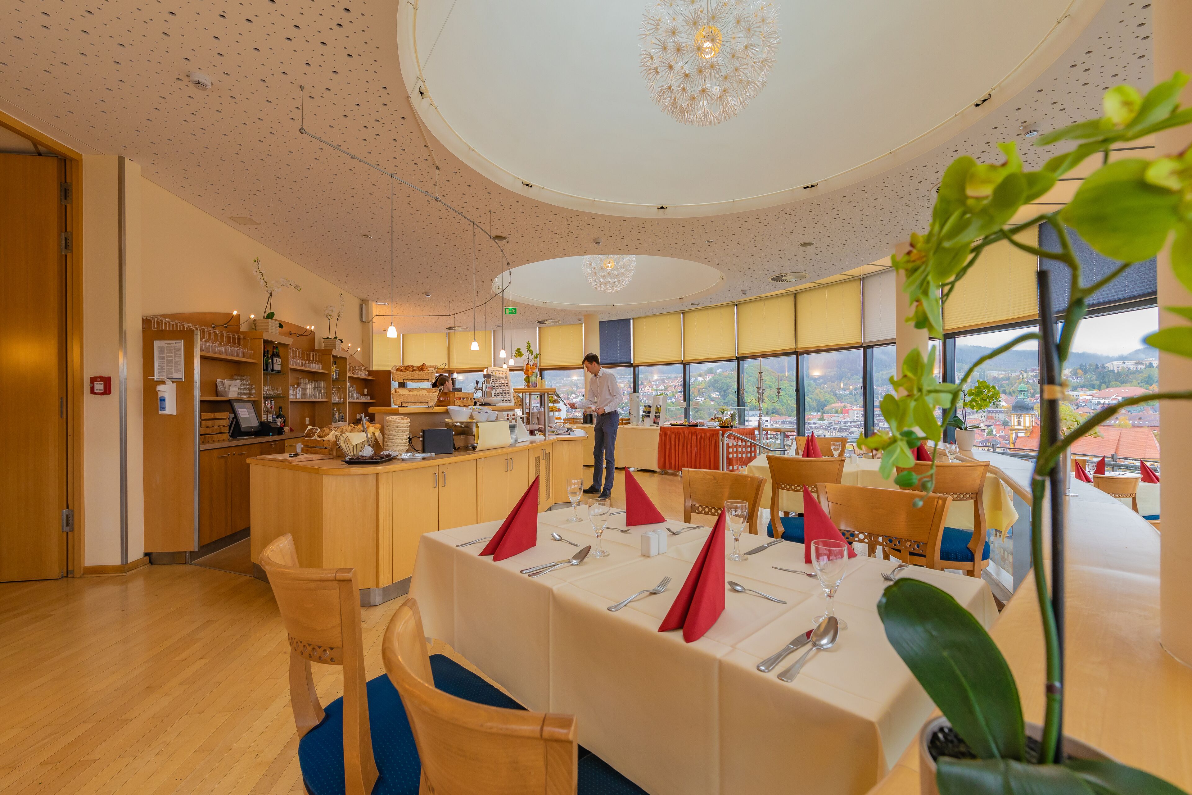 A restaurant with a high ceiling, wooden furniture, and a view of the city.