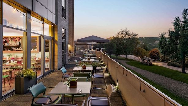 Un patio exterior con mesas y sillas, vista a la ciudad y un edificio con ventanas amplias.