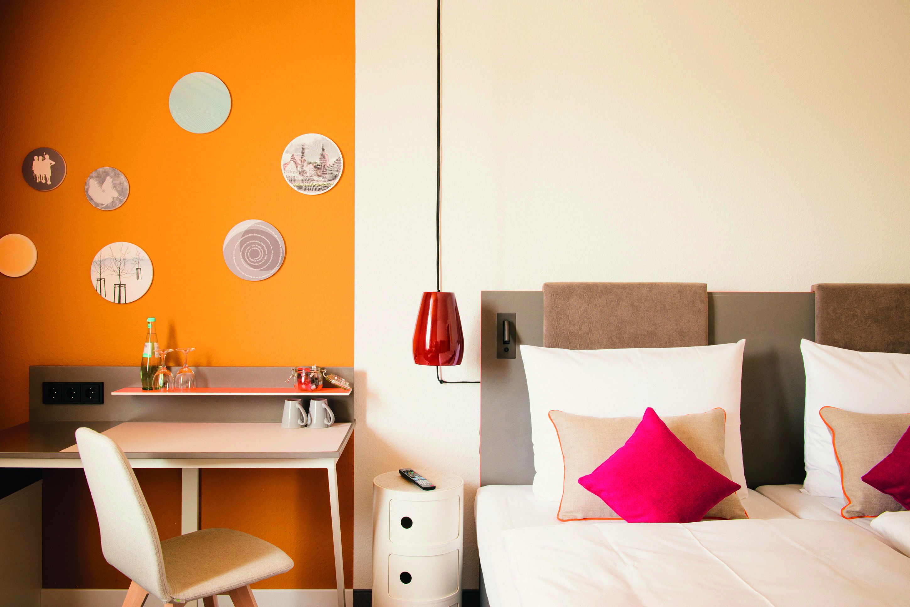 Una habitación de hotel con escritorio, cama con almohadas, lámpara roja y adornos en la pared.
