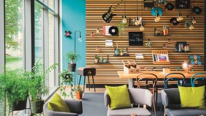 Un interior moderno con un revestimiento de listones de madera, plantas en macetas y una zona de comedor con sillas y mesas.