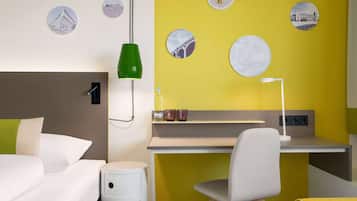 Ein modernes Hotelzimmer mit Bett, Schreibtisch, Stuhl und einer gelben Wand mit dekorativen Tellern.