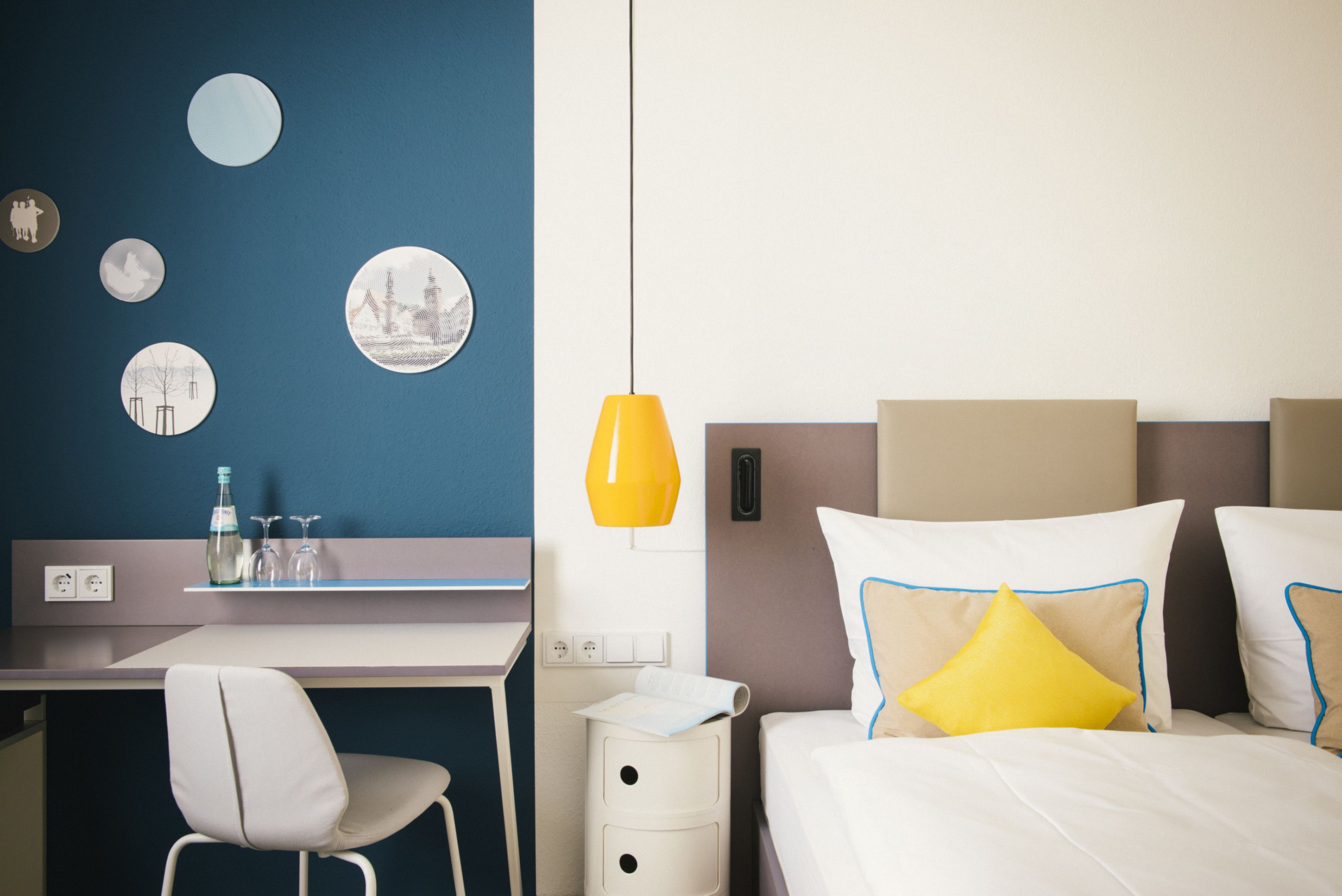 Ein Hotelzimmer mit Bett, Schreibtisch, Stuhl, Nachttisch und Wanddekorationen.