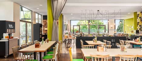 A modern restaurant with wooden tables and chairs, large windows, and a bright interior.