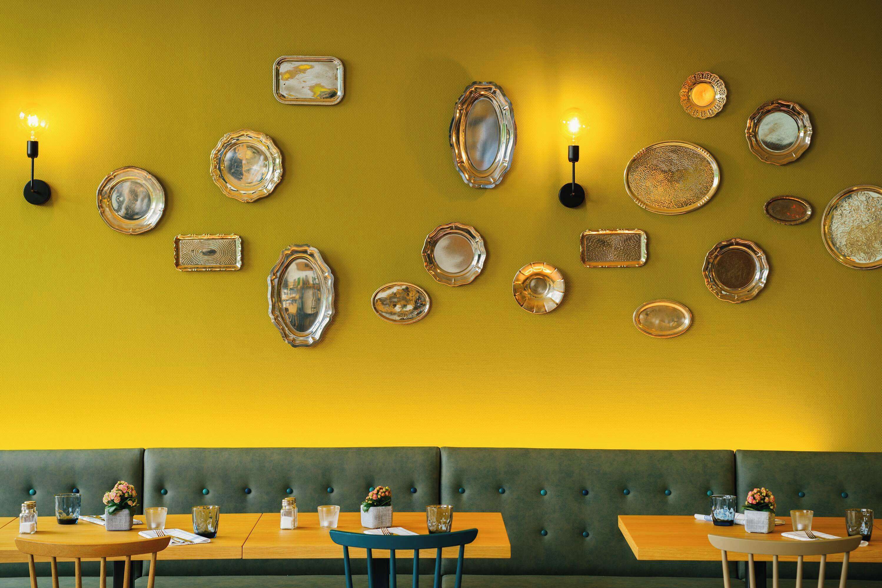 Ein Restaurantinneres mit gelber Wand, mehreren Tischen und einer grün gepolsterten Bank.