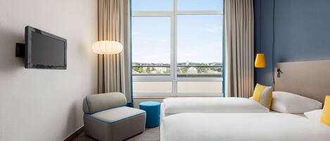 Habitación de hotel con un ventanal grande, un televisor de pantalla plana, un sofá, una cama y una lámpara.