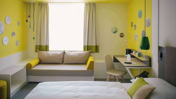 A hotel room with a bed, a desk, a chair, a sofa, and a window with curtains.