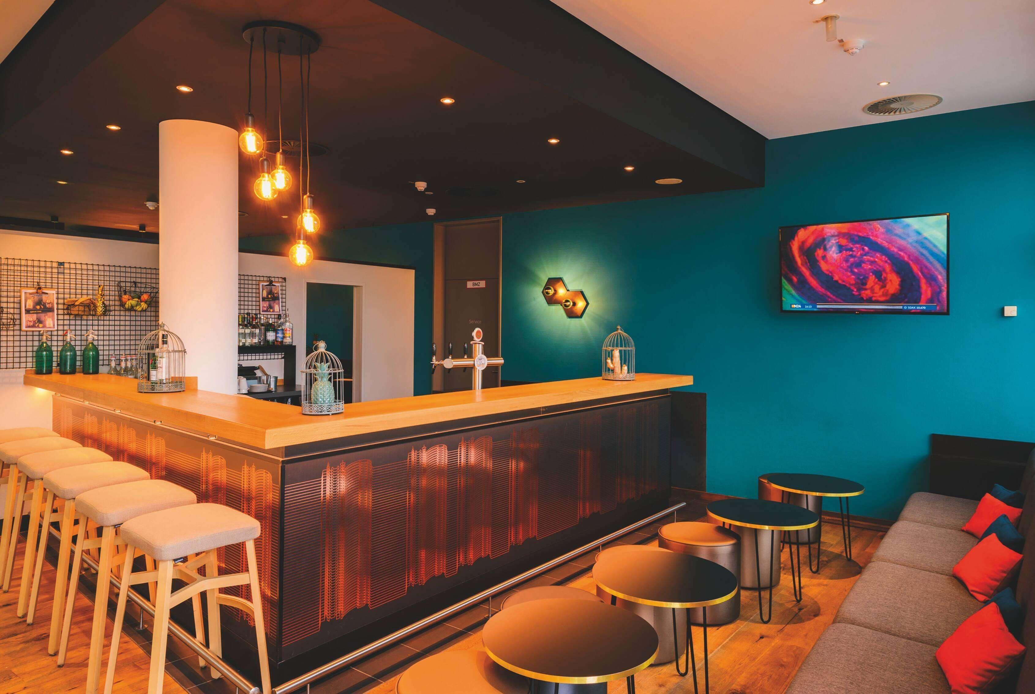 A bar area with stools, a counter, and a seating area with round tables and a sofa.
