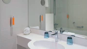 Une salle de bain moderne avec un lavabo blanc, deux récipients en verre bleu, une serviette et un miroir qui reflète l’espace de la douche.