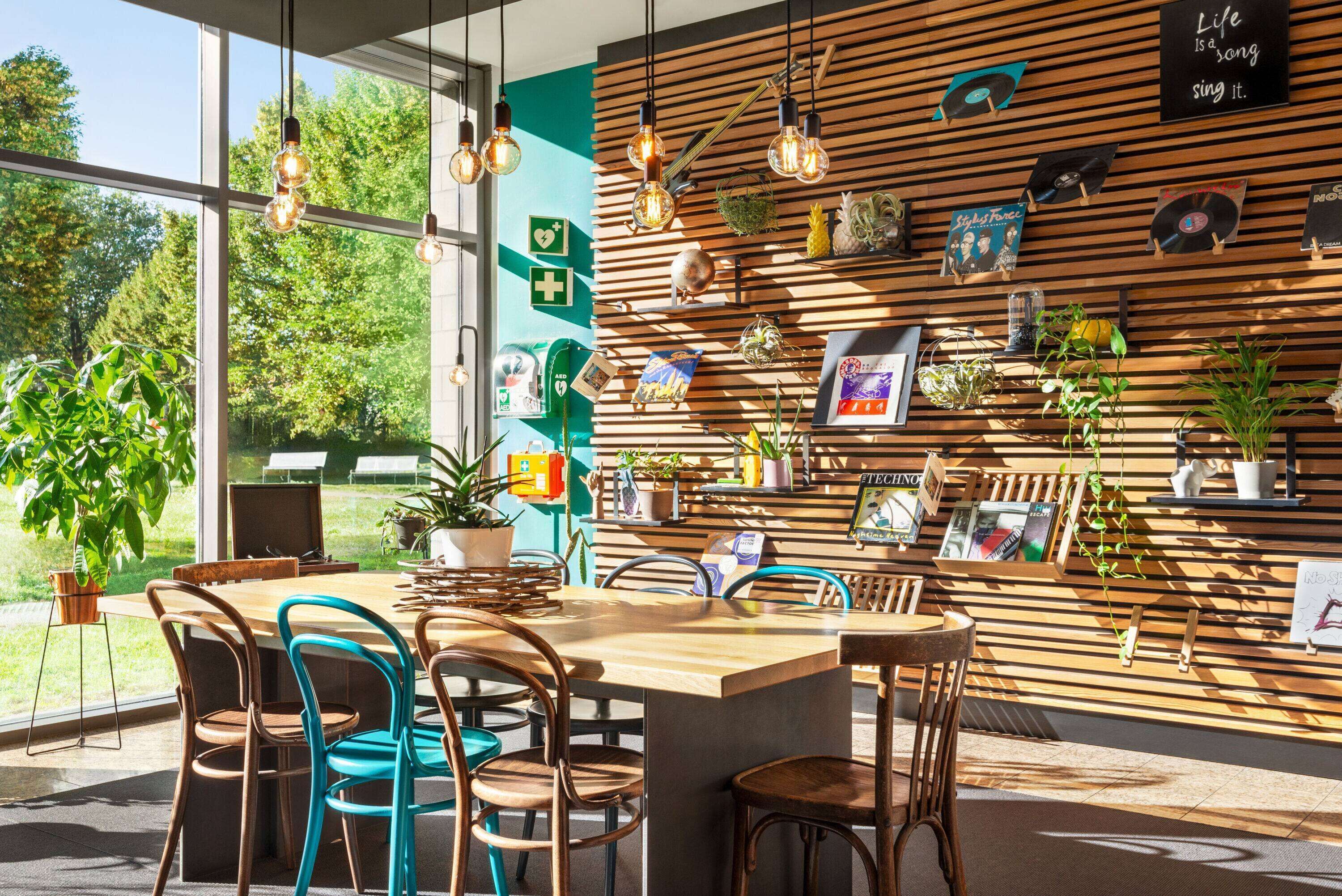 Una cafeteria moderna amb paret de lamelas de fusta, lluminàries penjants i diverses plantes.