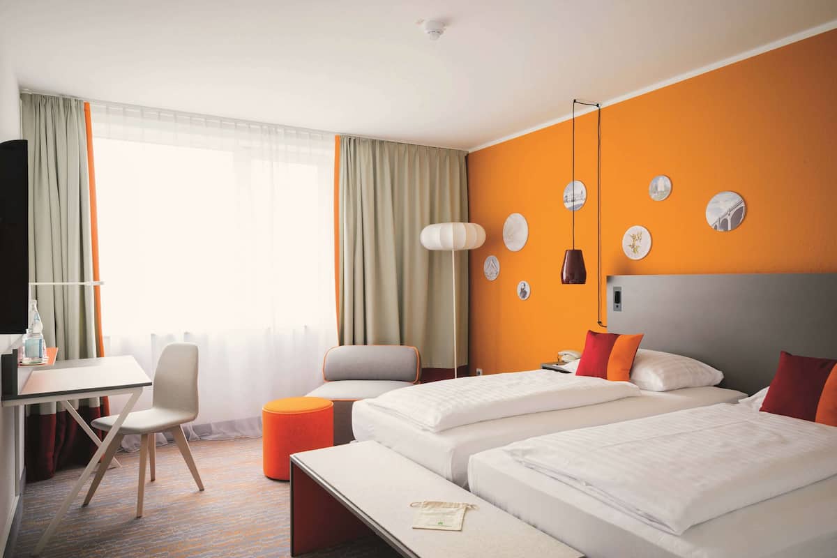 Habitación de hotel con dos camas, un escritorio, una silla y un pequeño taburete naranja.