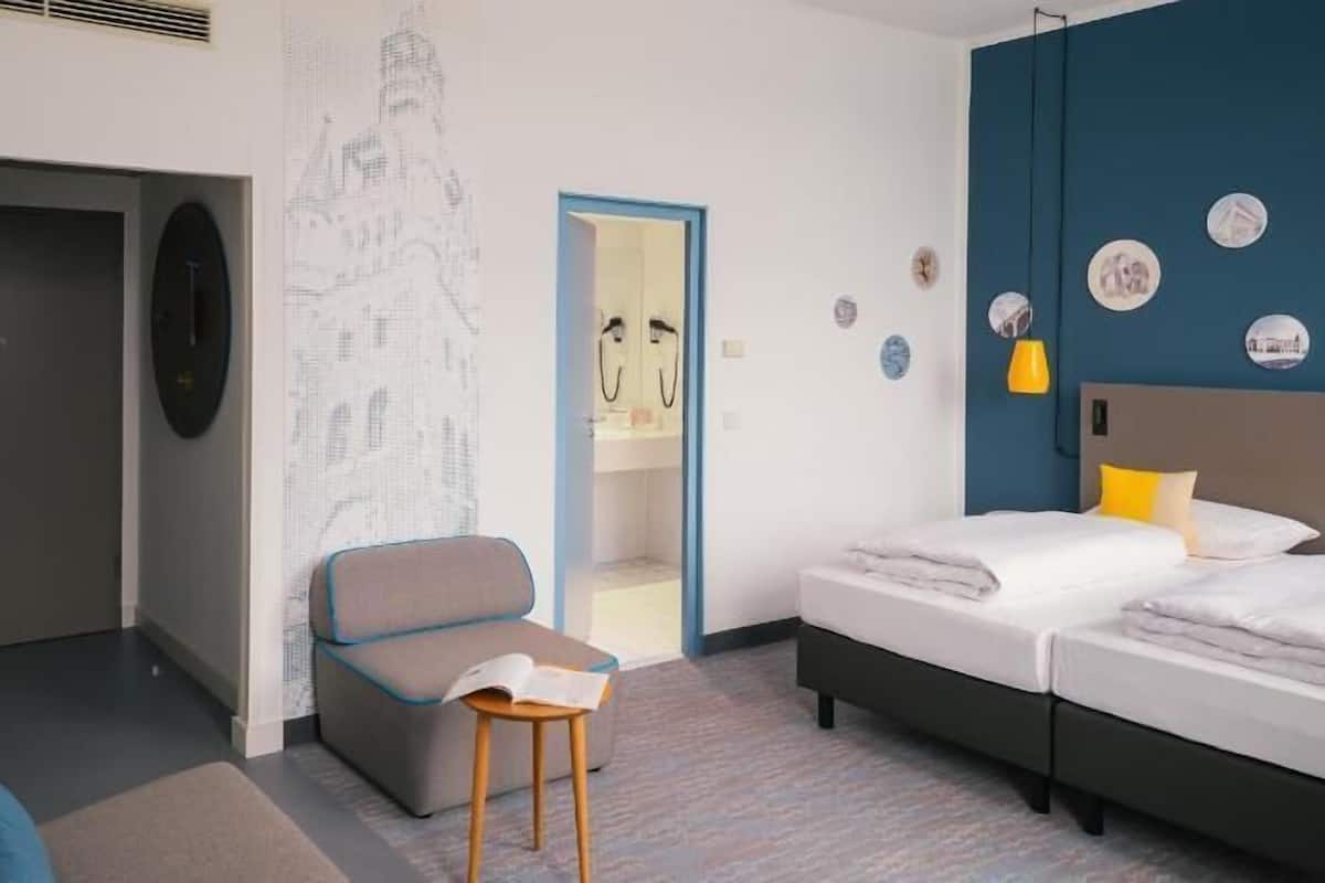 Una habitación de hotel con una cama, una silla, un escritorio y un armario.