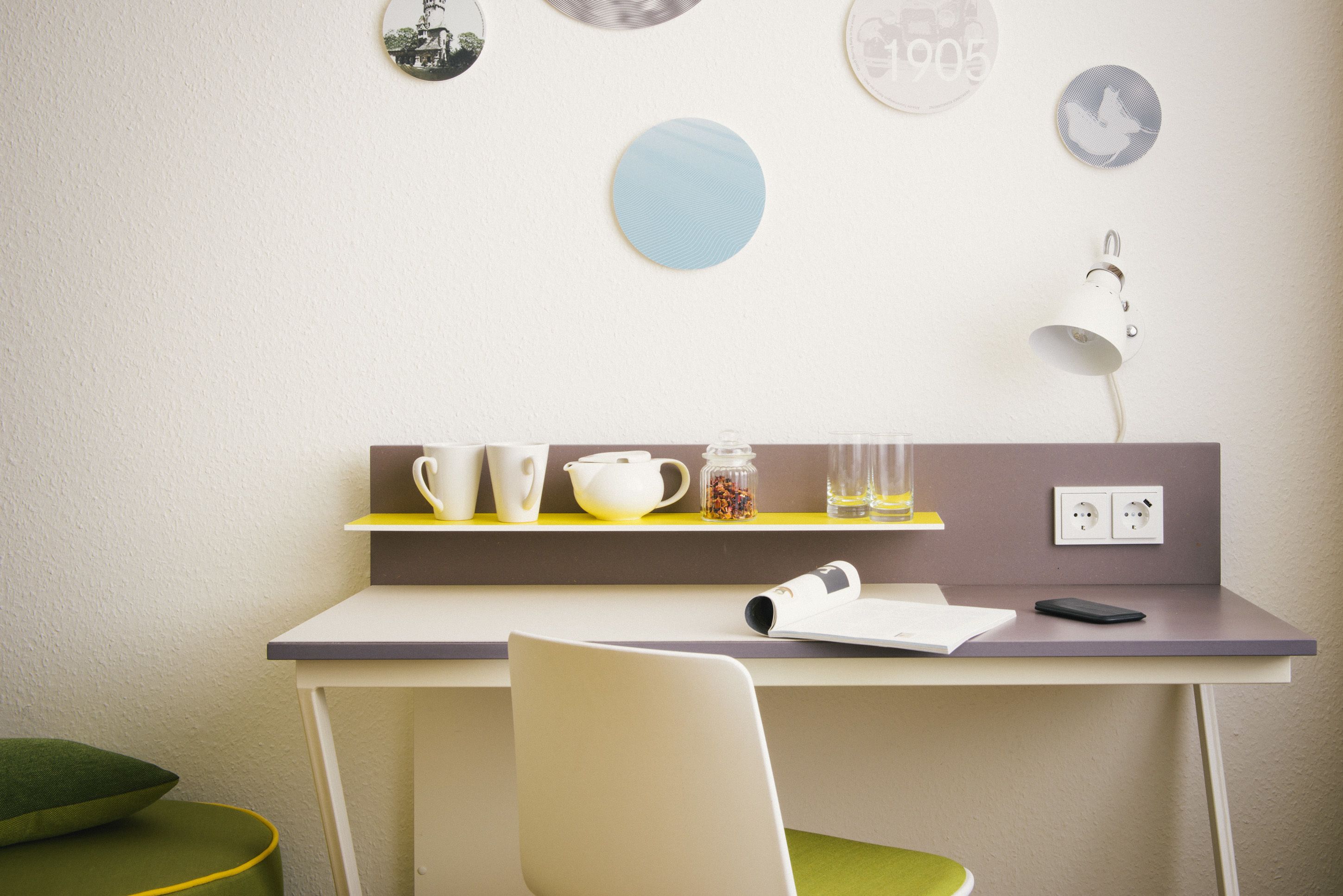 Una habitación moderna con un escritorio, una silla y una estantería con tazas, un hervidor y un tarro.