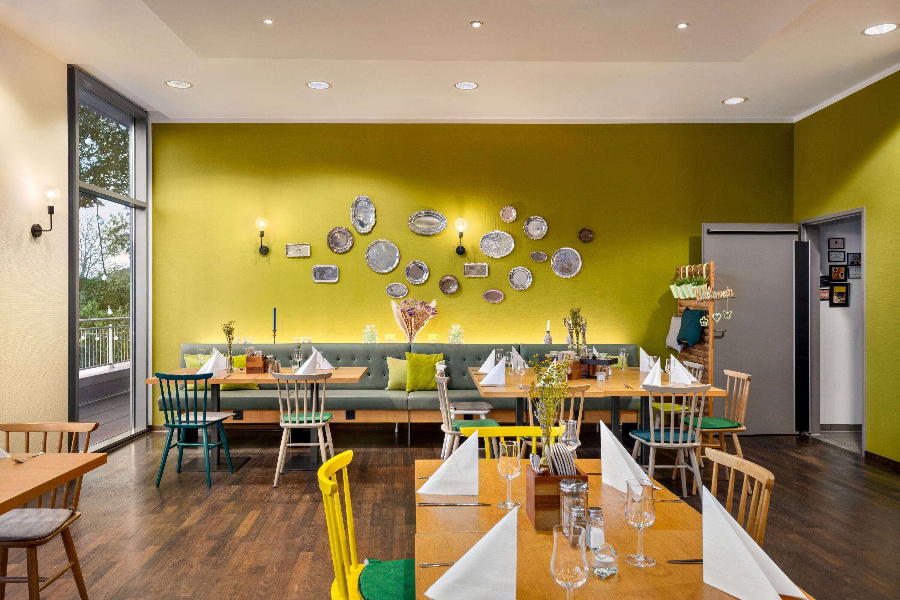 A restaurant with a green wall, wooden tables, and chairs.