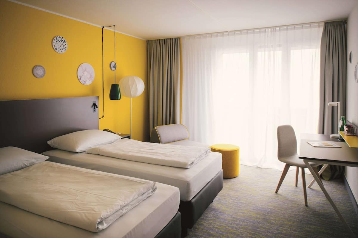 A hotel room with two beds, a desk, a chair, and a small round table.