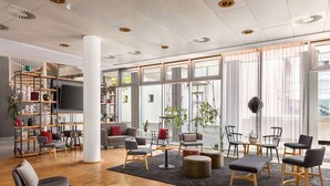 A modern interior with a central seating area, a bookshelf, and large windows. - Vienna House Easy by Wyndham Trier (Trier)