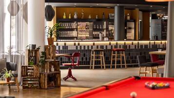 A bar area with a pool table, bar stools, and a variety of bottles and glasses.