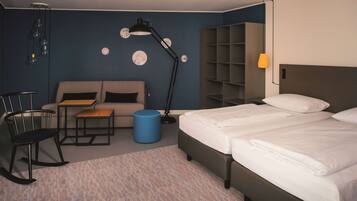 Quarto de hotel com cama, sofá, escrivaninha, cadeira e um banquinho azul.