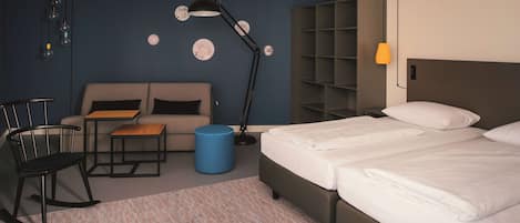 A hotel room with a bed, a sofa, a desk, a chair, and a blue ottoman.