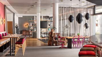 A modern interior with a long dining table, red and brown upholstered chairs, and a large window with sheer curtains.