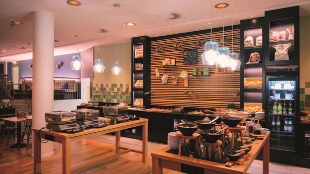 A bakery with wooden tables, shelves of baked goods, and a sign that says "GIVE US TODAY'S BREAD". - Vienna House Easy by Wyndham Trier (Trier)