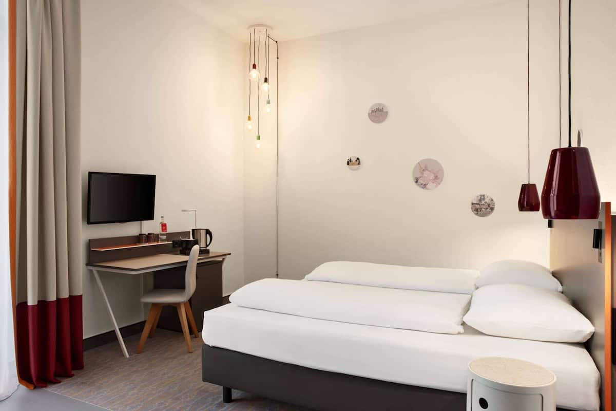 A hotel room with a bed, desk, chair, television, and wall decorations.