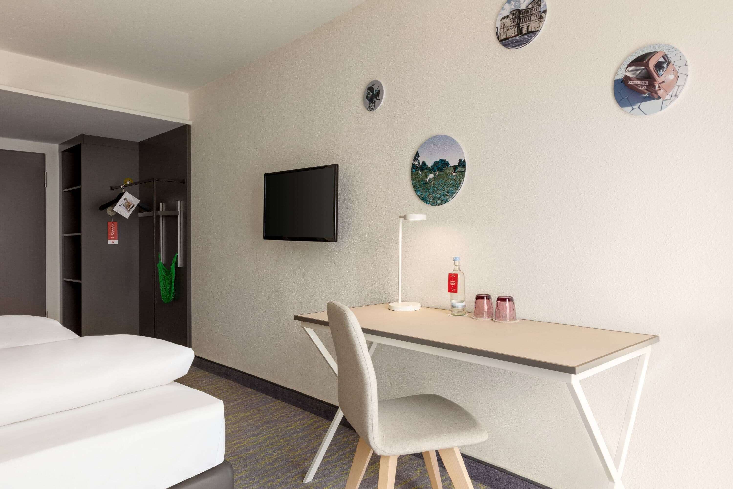 Een hotelkamer met een bed, een bureau met stoel, een flatscreen televisie en wanddecoraties.