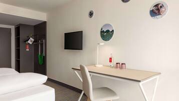 Une chambre d’hôtel comprenant un lit, un bureau avec une chaise, un téléviseur à écran plat et des éléments de décoration murale.