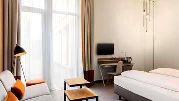 Una habitación de hotel moderna con sofá, una mesita de madera, cama, escritorio con silla, televisor y una lámpara de diseño original.