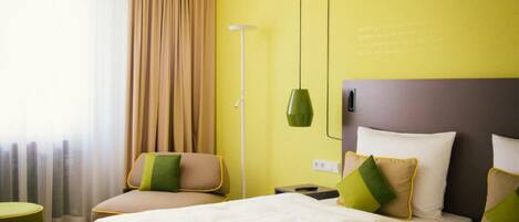 A hotel room with two beds, a green lamp, and a view of the outdoors through sheer curtains.