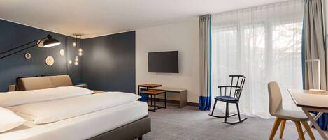 A hotel room with a large bed, a desk, a chair, a TV, and a window with curtains.