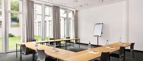A conference room with a long table, chairs, a whiteboard, and large windows with curtains.