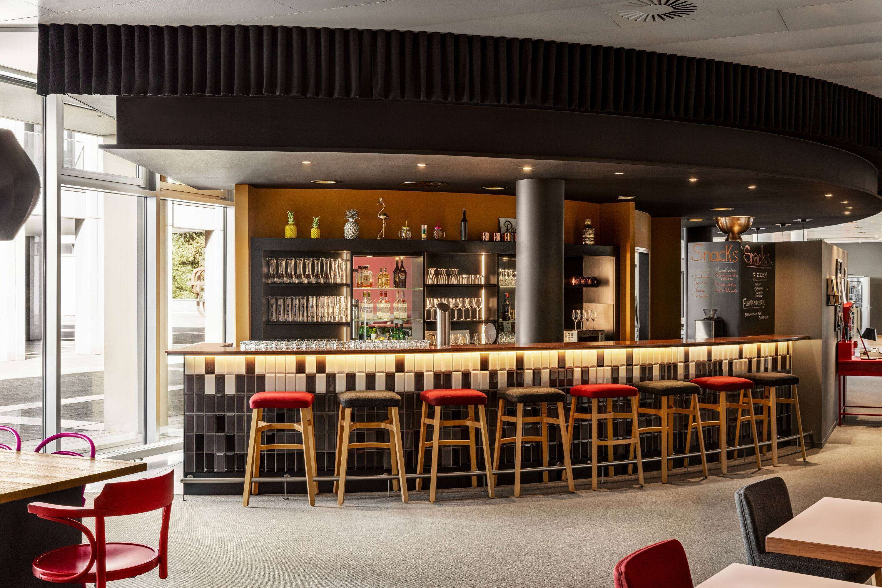 Un bar moderno con una barra curva, varios taburetes y una gran variedad de botellas y vasos a la vista.