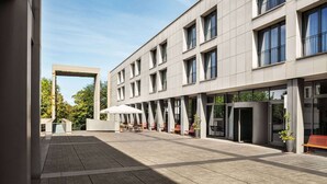 A modern building with a covered outdoor seating area, large windows, and a clear sky. - Vienna House Easy by Wyndham Trier (Trier)