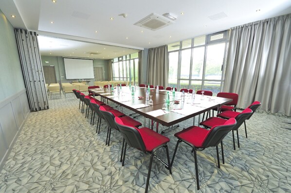 A conference room with a long table, red chairs, a projector screen, and large windows.