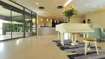 A spacious lobby with a grand piano, a reception desk, and a seating area.