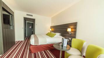A hotel room with a bed, a small table, a chair, and a TV mounted on the wall.
