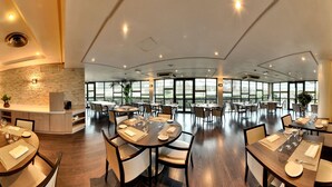 Un vaste espace dédié à la salle à manger, avec de nombreuses tables et chaises, de grandes fenêtres et un mur décoratif en pierre.