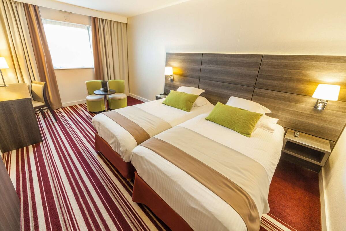 A hotel room with two beds, a desk, a chair, and a window with curtains.
