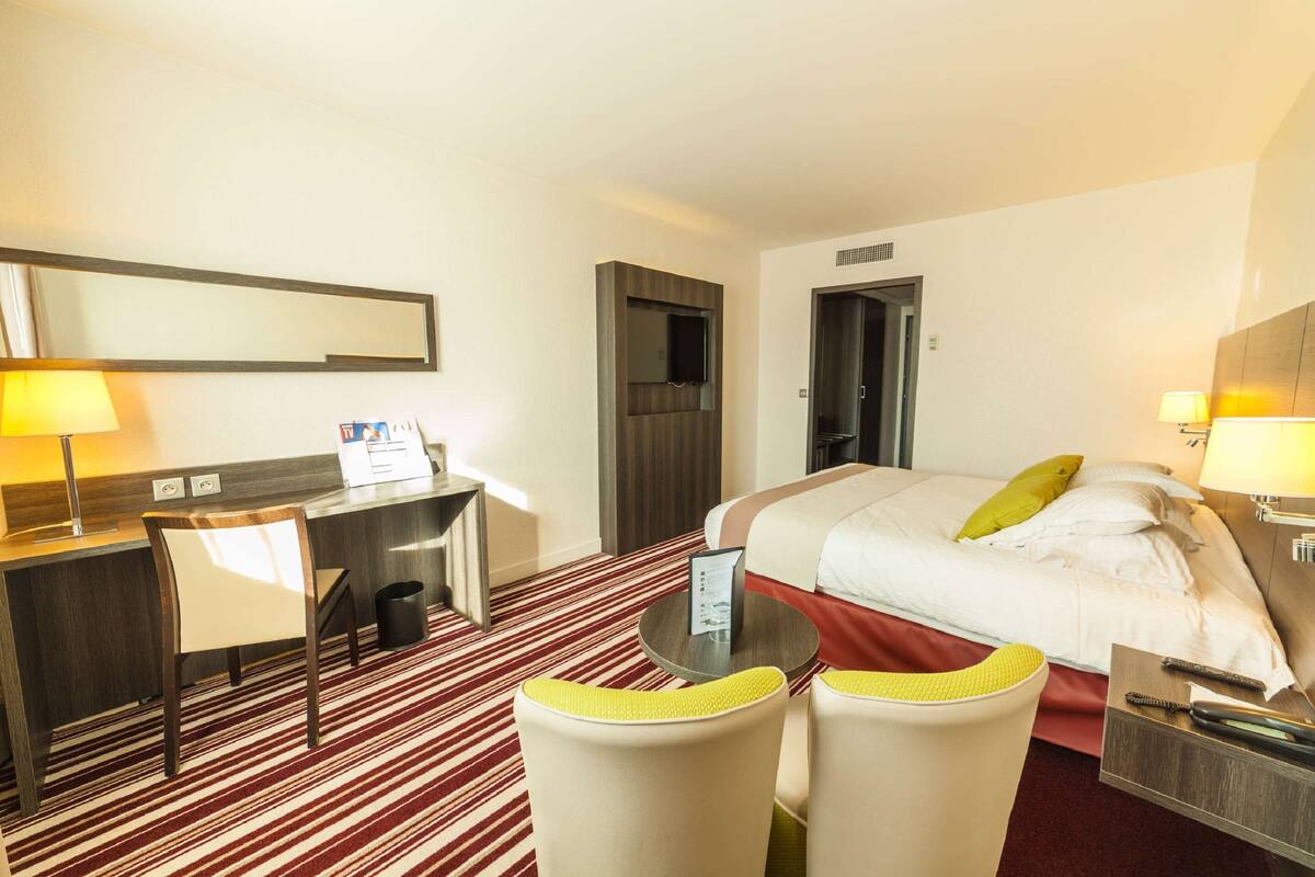 A hotel room with a bed, desk, chairs, and a mirror.
