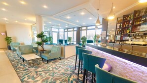 Un hall d’hôtel moderne doté d’un bar, de coins salon et de grandes fenêtres.