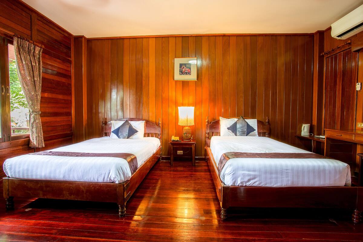 Una habitación de hotel con dos camas de madera, una mesita de noche con lámpara y un cuadro enmarcado en la pared.