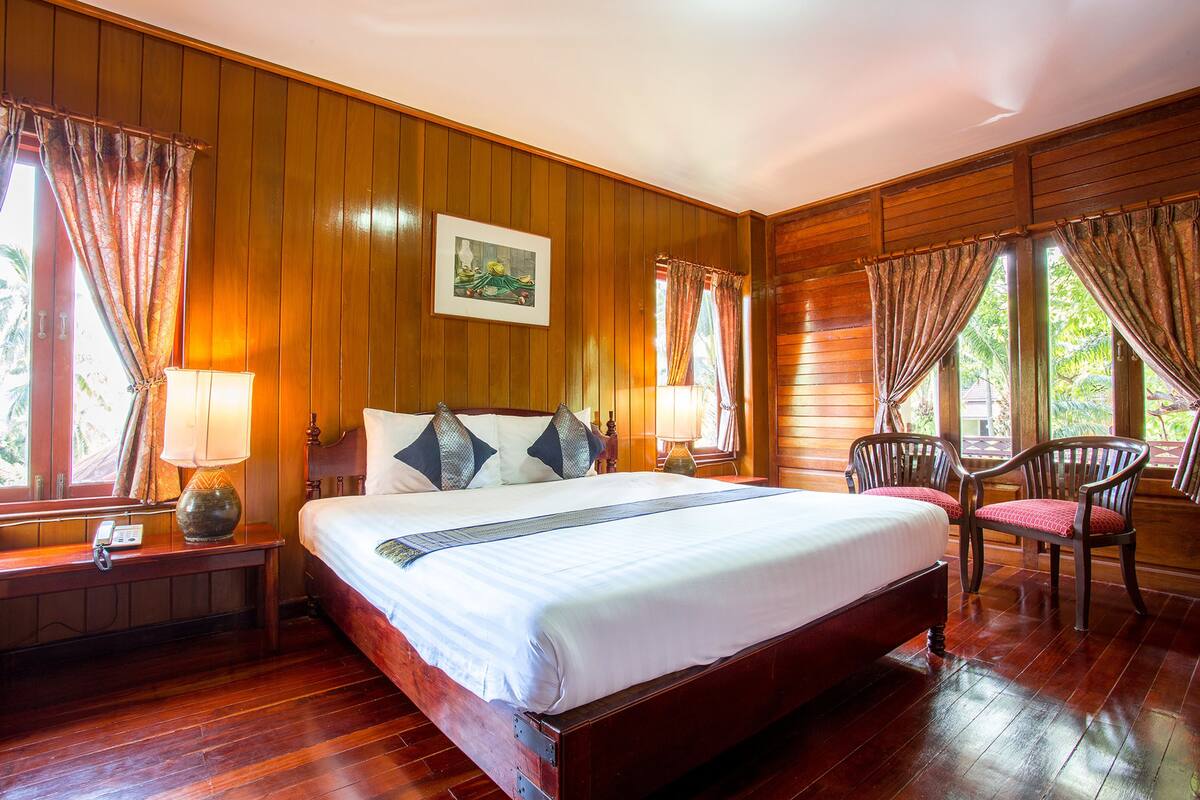 Una habitación con paneles de madera, una cama grande, dos sillones, una mesita de noche y una lámpara.