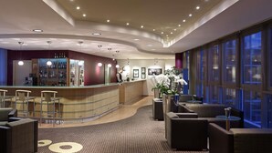 Un vestíbulo de hotel con un mostrador de recepción curvo, una zona de estar y grandes ventanales.