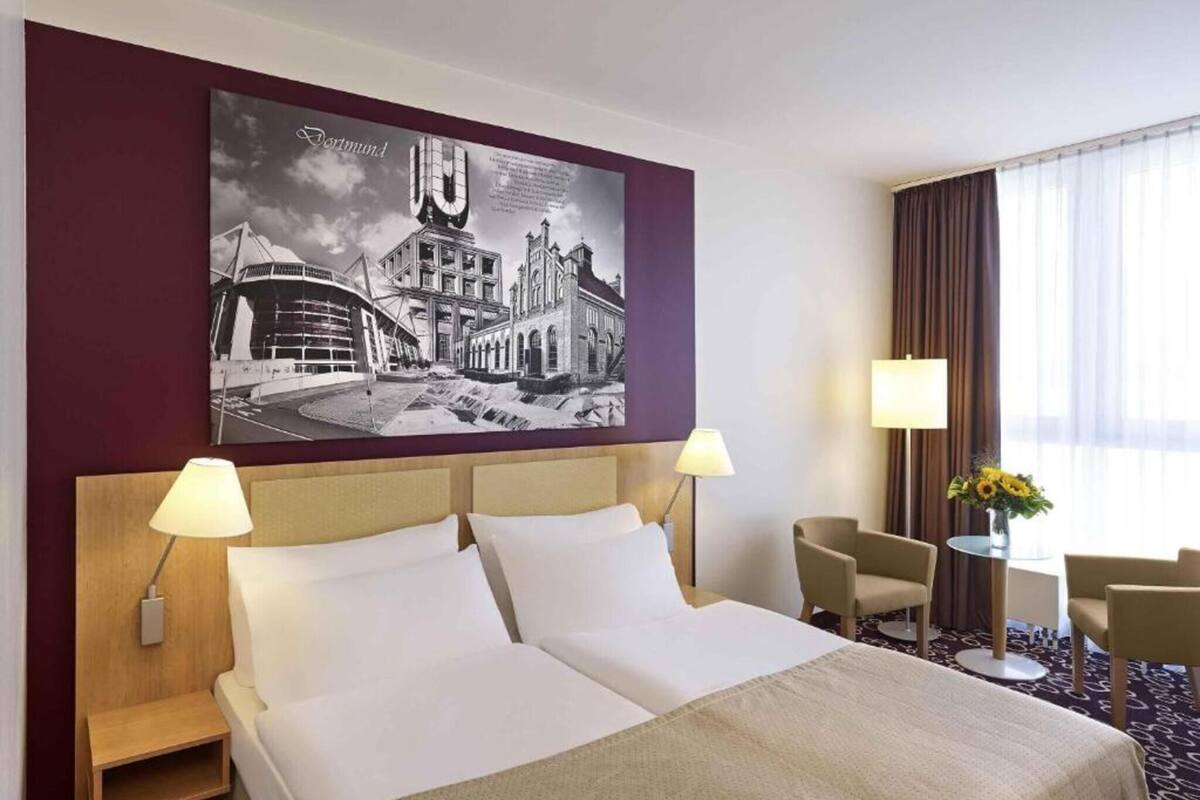 A hotel room with a large bed, two bedside tables, two lamps, a chair, and a wall-mounted artwork.