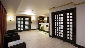 Un hall d’hôtel comprenant un comptoir d’accueil, deux tabourets de bar, un coin salon avec des fauteuils et des portes de style traditionnel dotées de panneaux de verre.